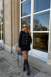 a lady wears a black cropped jacket with black shorts and knee-high boots